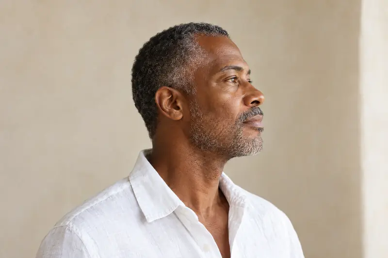Homem negro de barba grisalha, de perfil, com a linha da mandíbula e a região abaixo do queixo à luz da janela
