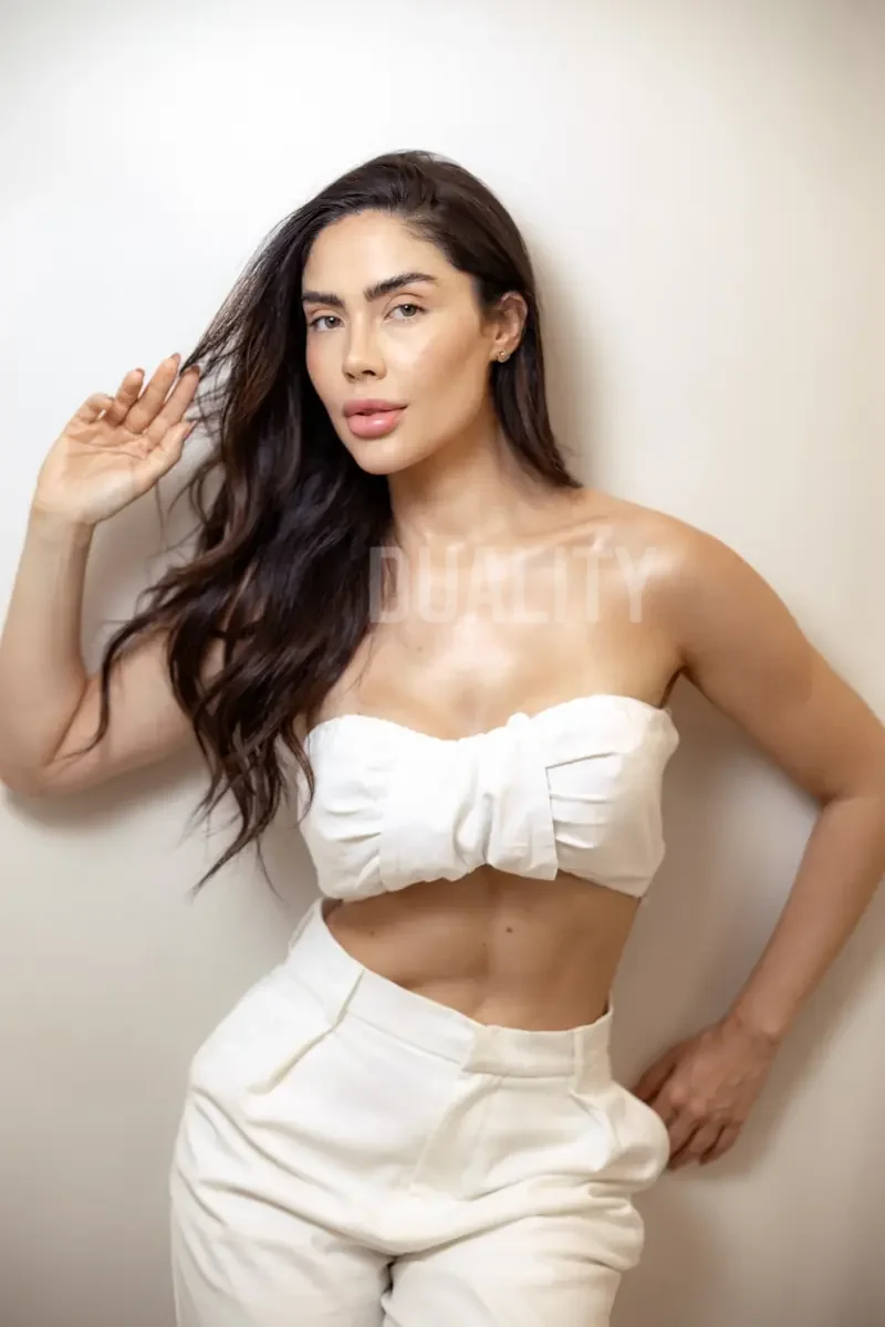 Mulher de top e calça brancos, com a mão no cabelo